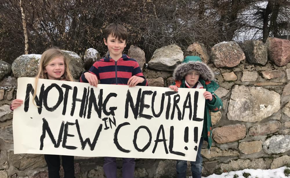 Three chidlren hold a placard reading "Nothing neutral in new coal" outside in the snow by a wall