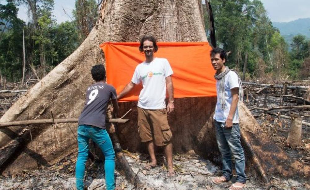 Alex standing in front of a giant tree, one of few remaining in the communal forest area at Tatai Leur in the Cardamom mountain forests. This tree blessing ceremony with villagers and Buddhist monks in 2013 sparked a wave of direct action which led to the