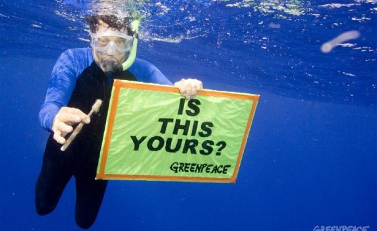 Man in sea with plastic and "is this yours?" sign.